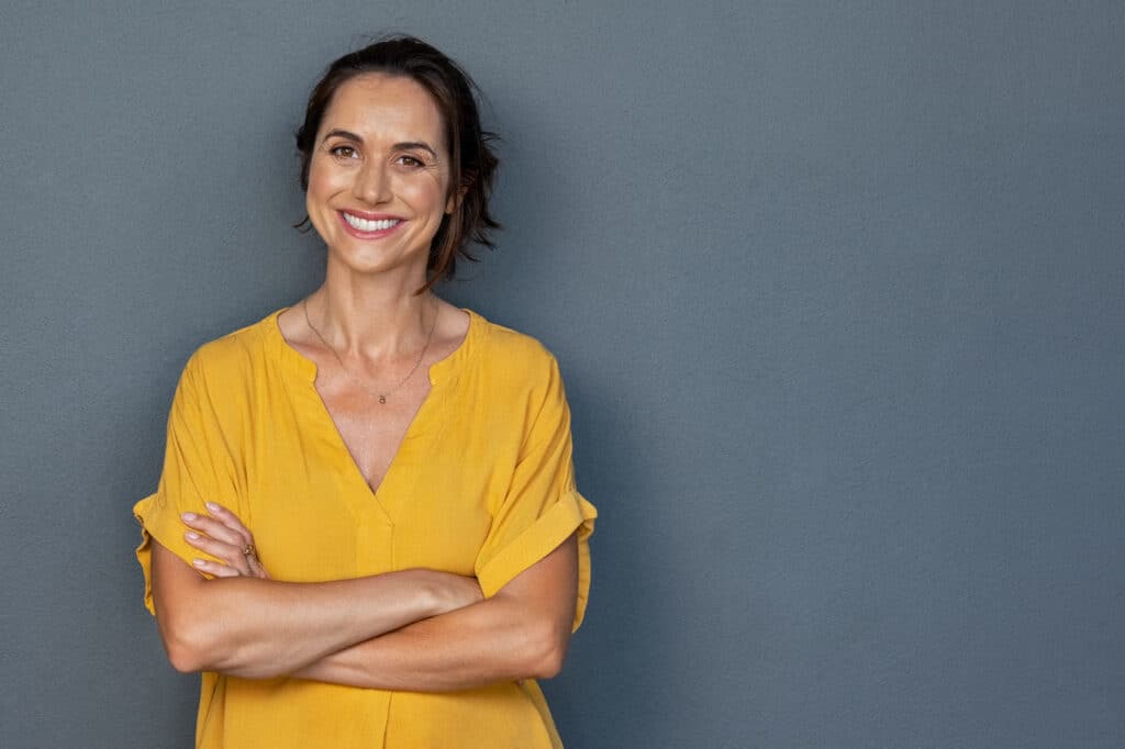 Smiling woman in a yellow blouse with her arms crossed