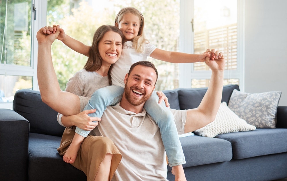 Laughing family on a sofa, the father carrying their daughter on his shoulders
